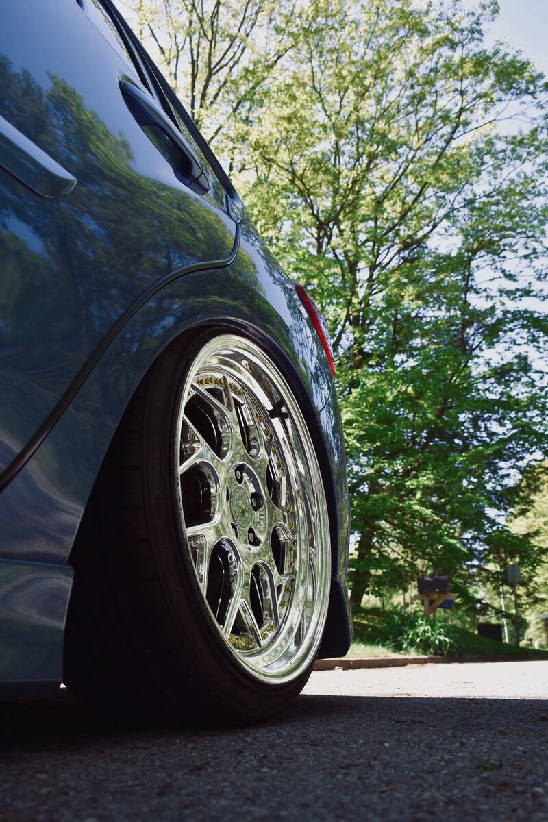 Low angle close-up of a polished multi-piece wheel with gold hardware tucked under a lowered fender