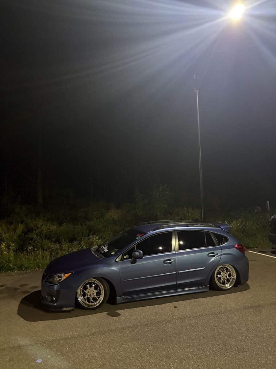 Lowered blue Subaru Impreza hatchback parked under a light at night